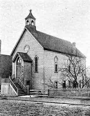 Two story frame building, enclosed porch with double doors; small square bell-tower on roof.